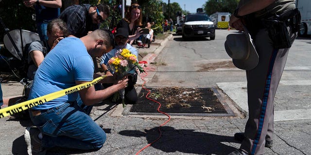 Joseph Avila, left, prays while holding flowers honoring the victims killed in Tuesday's shooting at Robb Elementary School in Uvalde, Texas, Wednesday, May 25, 2022.