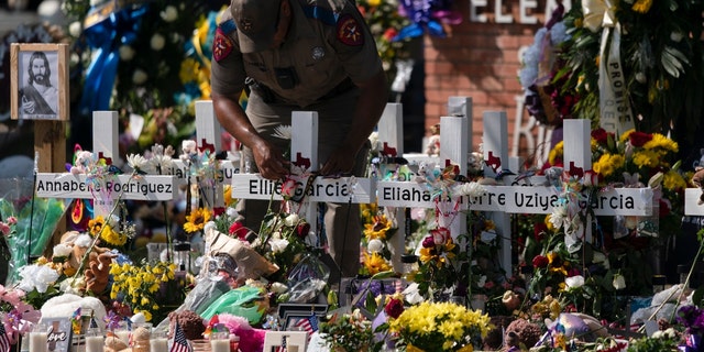 A state trooper places a tiara on a cross honoring Ellie Garcia, one of the victims killed in this week's elementary school shooting in Uvalde, Texas Saturday, May 28, 2022. 