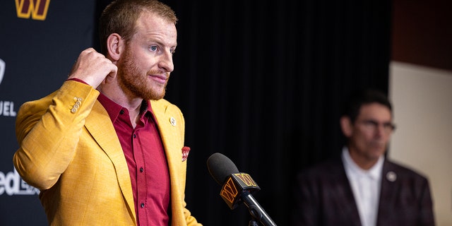 Quarterback Carson Wentz of the Washington Commanders is introduced, and head coach Ron Rivera looks on at Inova Sports Performance Center March 17, 2022, in Ashburn, Va.