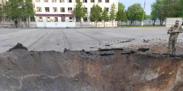 A uniformed soldiers stands around a crater in the middle of a courtyard in Desna, Ukraine, on Tuesday, May 17.