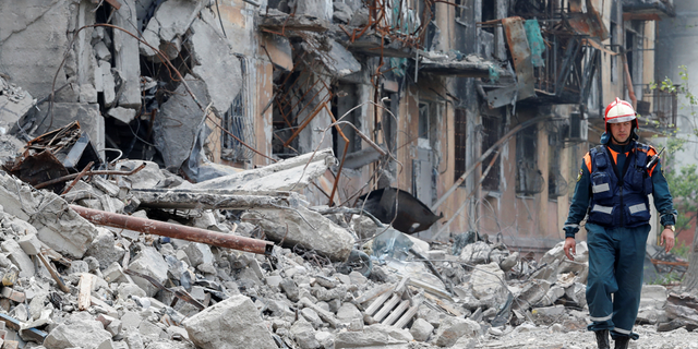 A member of Russia's Emergencies Ministry walks near a destroyed residential building in Mariupol, Ukraine, on Thursday, May 11.