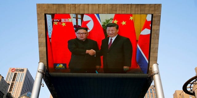 People bicycle past a giant TV screen broadcasting the meeting of North Korean leader Kim Jong Un and Chinese President Xi Jinping during a welcome ceremony at the Great Hall of the People in Beijing.