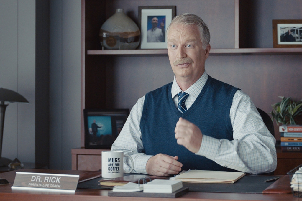 Actor Bill Glass as "Dr. Rick" in the Progressive Insurance ads. He's wearing a sweater-vest and sitting at a desk.