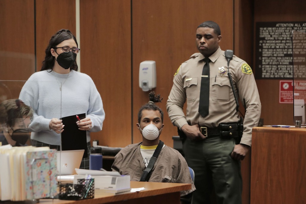 Lee shown seated in court. His attorney and a court officer stand behind him.