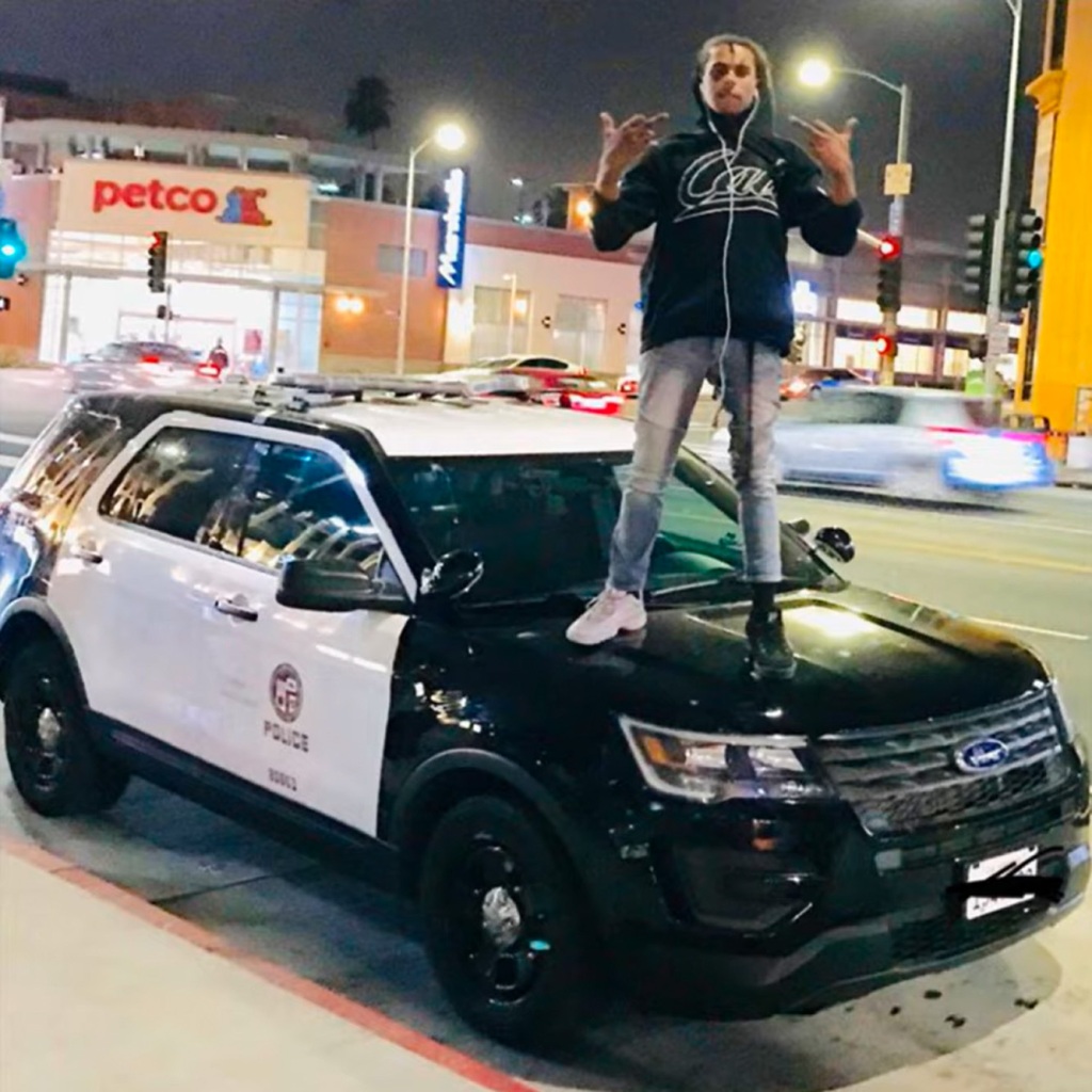 Isaiah Lee, aka rapper Noname Trapper," is seen in a Youtube photo for his song "Dave Chappell." He is seen standing on a police car, in jeans, a hoodie and sneakers that do not match.