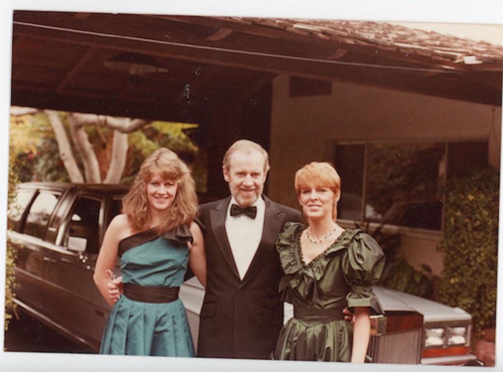 George Carlin with his daughter, Kelly, and his wife, Brenda. It appears to be a photograph from the 1970s; they're outside standing in front of a Cadillac limousine.