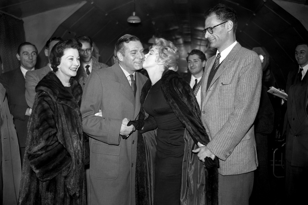 Marilyn Monroe greets English actor Sir Laurence Olivier with a kiss on the cheek, watched by his wife Vivien Leigh (left) and Monroe's husband Arthur Miller (right).