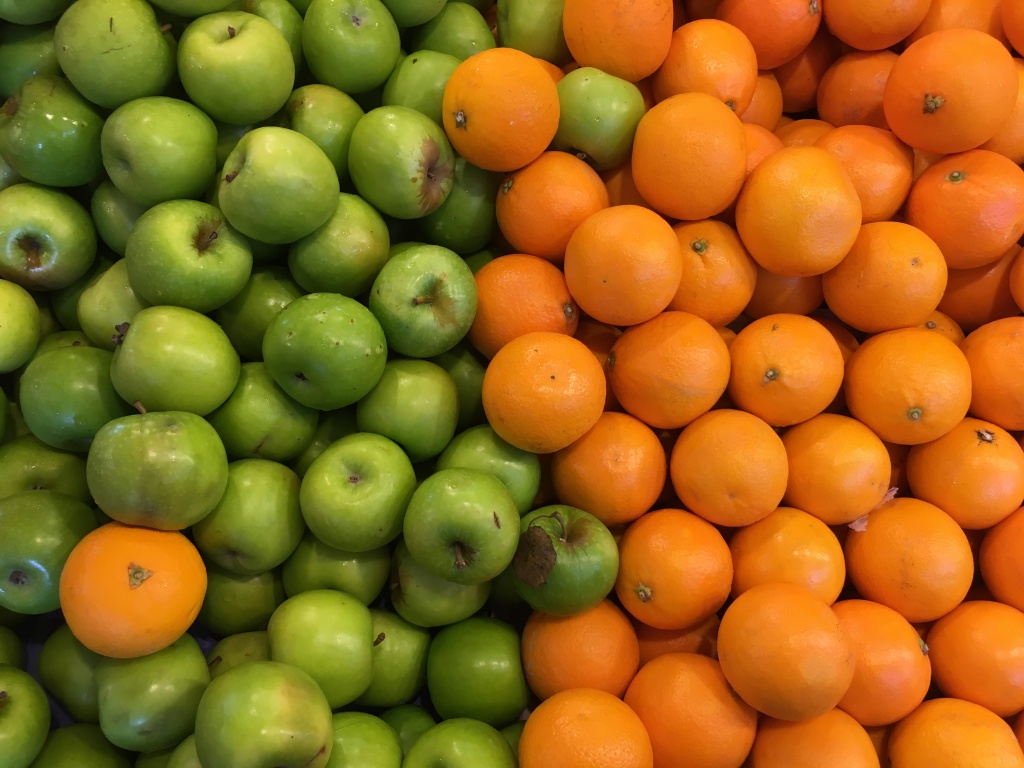 A large pile of green apples and oranges.