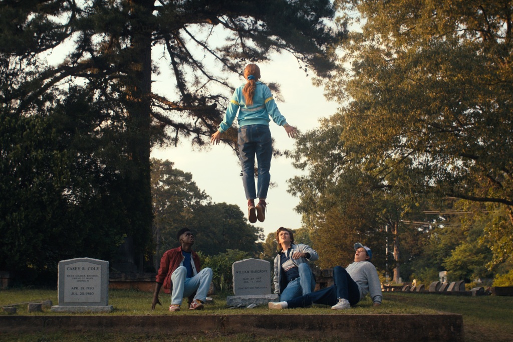 Lucas (Caleb McLaughlin), Max (Sadie Sink), Steve (Joe Keery) and Dustin (Gatem Matarazzo) gather around a grave while Max levitates. 