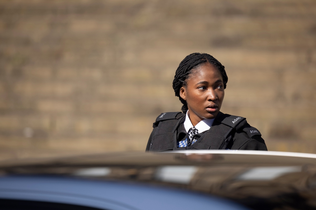 Adelayo Adedayo as Chris' partner, Rachel Hargreaves. She's standing next to a police car and is looking off to the side.