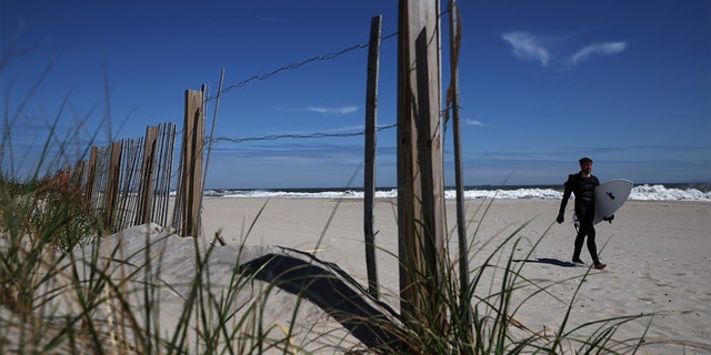 A man carries his surfboard after surfing in the Atlantic Ocean along the beach in Long Beach, New York, May 9, 2022.