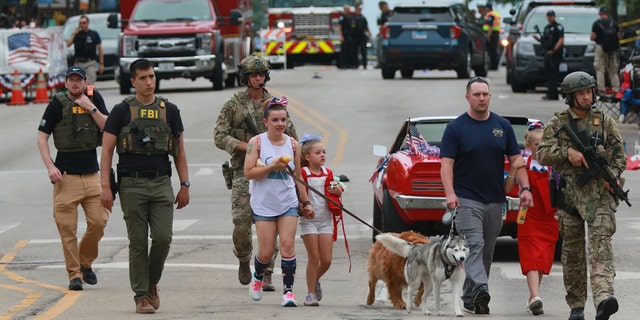 HIGHLAND PARK, ILLINOIS - JULY 04: Law enforcement escorts a family away from the scene of a shooting at a Fourth of July parade on July 4, 2022 in Highland Park, Illinois. Police have detained Robert "Bobby" E. Crimo III, 22, in connection with the shooting in which six people were killed and 19 injured, according to published reports.  