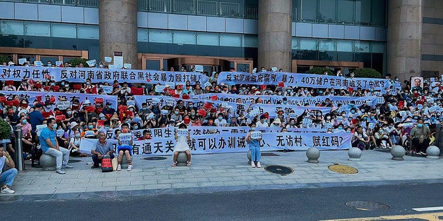 People hold banners and chant slogans during a protest at the entrance to a branch of China's central bank in Zhengzhou on Sunday, July 10. A large crowd of angry Chinese bank depositors faced off with police, some reportedly injured as they were roughly taken away, in a case that has drawn attention because of earlier attempts to use a COVID-19 tracking app to prevent them from mobilizing. (AP Photo/Yang)