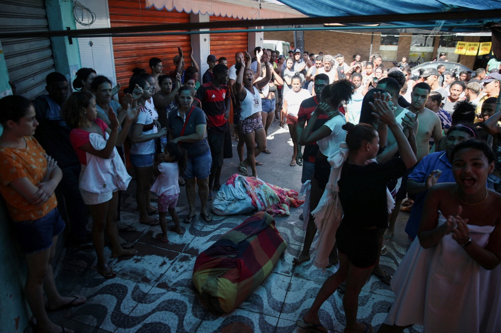 Residents stand next to dead bodies during a police operation against drug gangs in Alemao slums complex on July 21, 2022. 