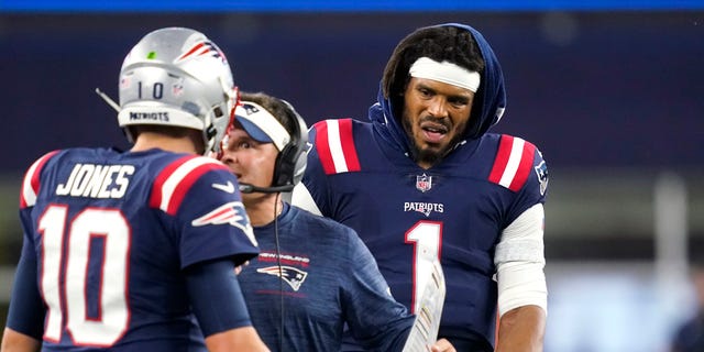 New England Patriots quarterback Cam Newton (1) looks on as offensive coordinator Josh McDaniels talks with quarterback Mac Jones during the first half of the team's preseason game against Washington, Aug. 12, 2021, in Foxborough, Massachusetts.