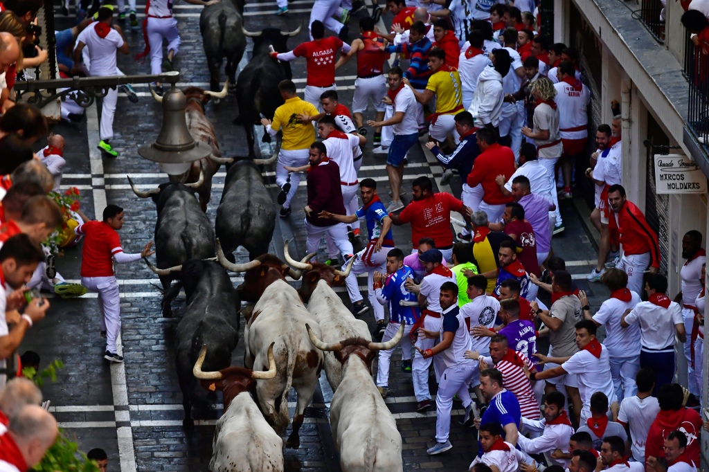 People run in the street as the bulls are seen charging up the middle of the road at the San Fermin Festival in Pamplona, northern Spain on July 9, 2022. 