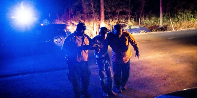 Firefighters help an elderly man from his car, seen at right, after he crashed into a ditch while driving away from the Oak Fire in Mariposa County, Calif., on Friday, July 22, 2022.