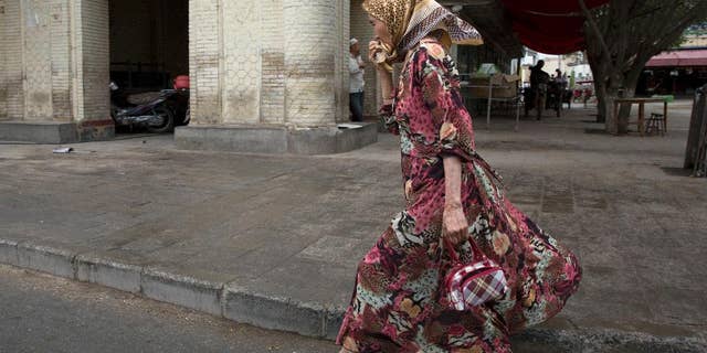 A Uyghur woman walks past a mosque in the city of Kuqa in western China's Xinjiang province.  In China's restive western province of Xinjiang, young men of the Uighur ethnic minority are not allowed to have beards. Also proscribed are certain types of women's headscarves, veils and "jilbabs," loose, full-length garments worn in public. (AP Photo/Ng Han Guan)