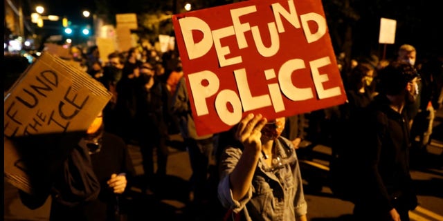 Demonstrators hold a sign reading "Defund the police."