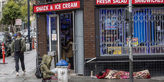 A person experiencing homelessness sleeps on the sidewalk in the Tenderloin district of San Francisco, California, on Thursday, April, 14, 2022. 