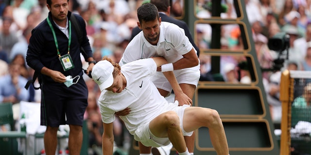 Novak Djokovic of Serbia helps Jannik Sinner of Italy after they slipped and fell during their Men's Singles Quarter Final match on day nine of The Championships Wimbledon 2022 at All England Lawn Tennis and Croquet Club on July 05, 2022 in London, England. 