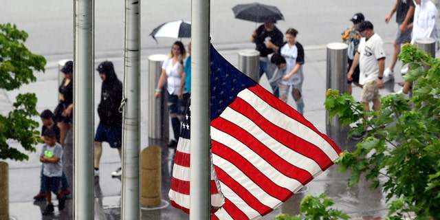 A United States flag flies at half-staff after a Fourth of July parade shooting in nearby Highland Park, Ill., while lines of fans wait to go through added security at Guaranteed Rate Field, Monday, July 4, 2022, in Chicago before a baseball game between the Chicago White Sox and the Minnesota Twins.