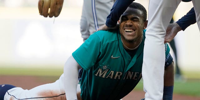 Seattle Mariners' Julio Rodriguez is helped up by third base coach Manny Acta after Rodriguez was tagged out at third by Toronto Blue Jays third baseman Matt Chapman after Rodriguez tripped on the way to third after hitting a double during the first inning of a baseball game, Friday, July 8, 2022, in Seattle. 