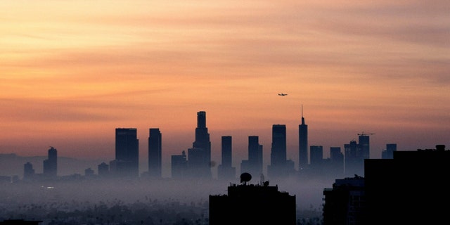 A plane flies over the Los Angeles, California, skyline at sunrise on March 25, 2022. 