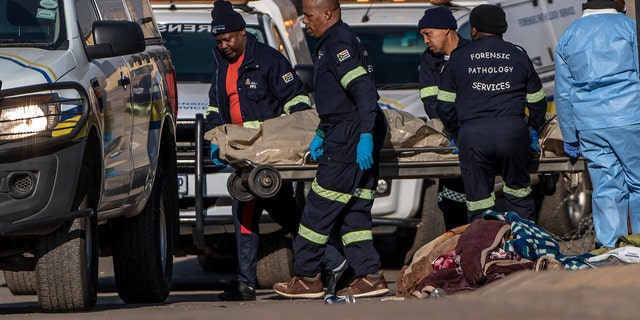 A body is removed from the scene of an overnight bar shooting in Soweto, South Africa, Sunday July 10, 2022. A mass shooting at a tavern in Johannesburg's Soweto township has killed 15 people and left others in critical condition, according to police. Police say they are investigating reports that a group of men arrived in a minibus taxi and opened fire on some of the patrons at the bar shortly after midnight Sunday. (AP Photo/Shiraaz Mohamed)