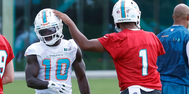 Tua Tagovailoa (1) taps the helmet of Tyreek Hill (10) of the Miami Dolphins between drills during at mandatory minicamp at the Baptist Health Training Complex June 1, 2022, in Miami Gardens, Fla.