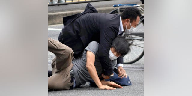 Tetsuya Yamagami, bottom, is detained near the site of gunshots in Nara Prefecture, western Japan, Friday, July 8, 2022.