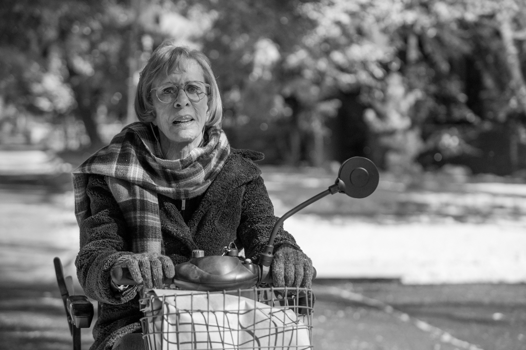 Carol Burnett as Marion. She's sitting outside on a motorized scooter. She's wearing a scarf, heavy coat and gloves and looks worried.