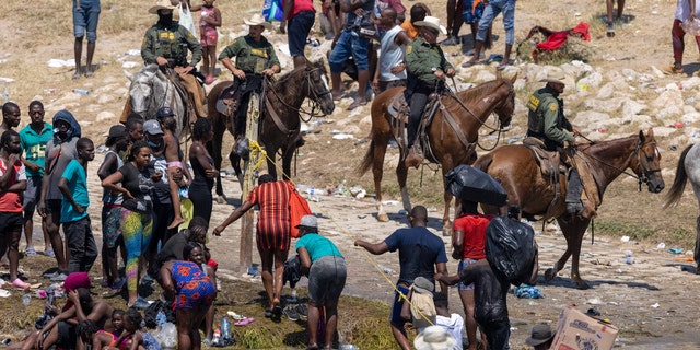 Mounted U.S. Border Patrol agents watch Haitian immigrants on the bank of the Rio Grande in Del Rio, Texas, Sept. 20, 2021, as seen from Ciudad Acuna, Mexico.