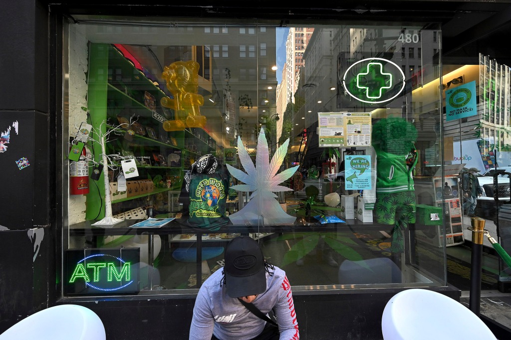 A man sitting outside of 'Weed World Candies' prepares to smoke cannabis