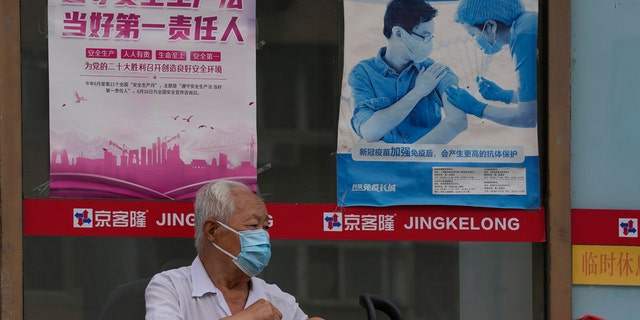 An elderly man wearing a mask waits near a poster promoting vaccination, Tuesday, July 19, 2022, in Beijing.