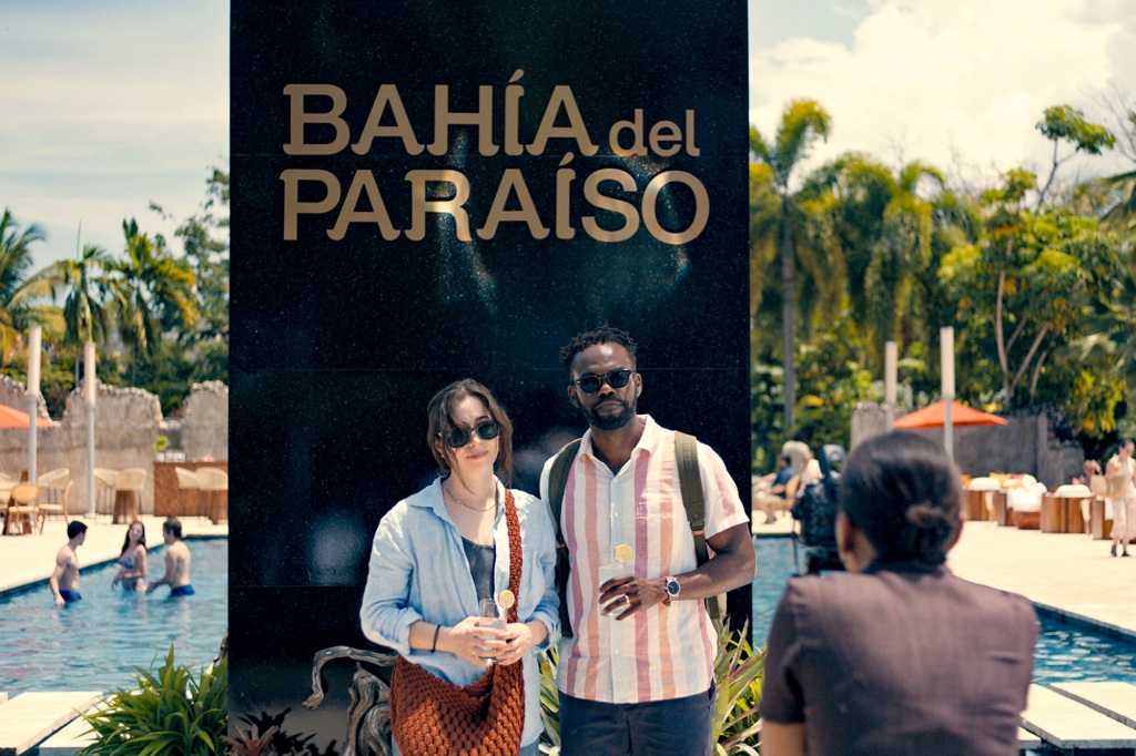 Emma (Cristin Milioti) and Noah (William Jackson Harper) pose for a picture while checking into their resort. 