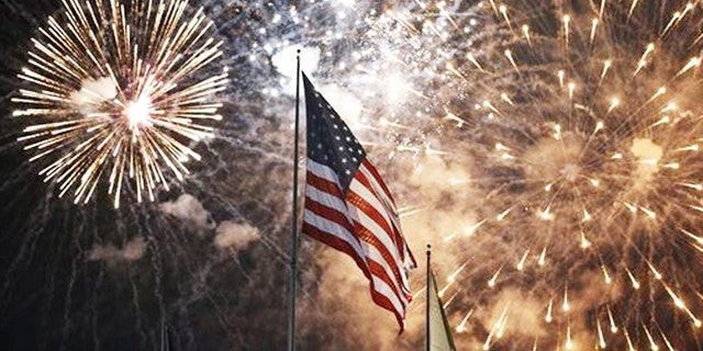 Fireworks explode behind a United States flag during a Fourth of July celebration at State Fair Meadowlands, East Rutherford, N.J.