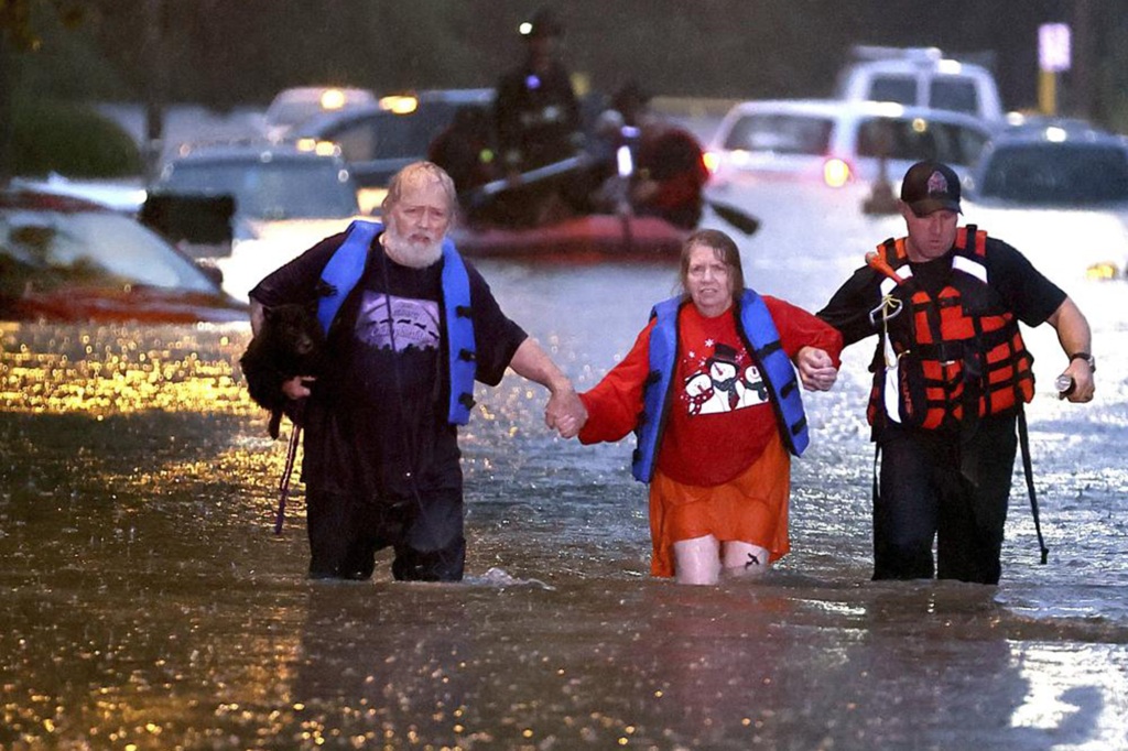 John Ward, left, and a firefighter help Lynn Hartke wade through the flash floodwater on Hermitage Avenue in St. Louis on Tuesday, July 26, 2022. (David Carson/St. Louis Post-Dispatch via AP)