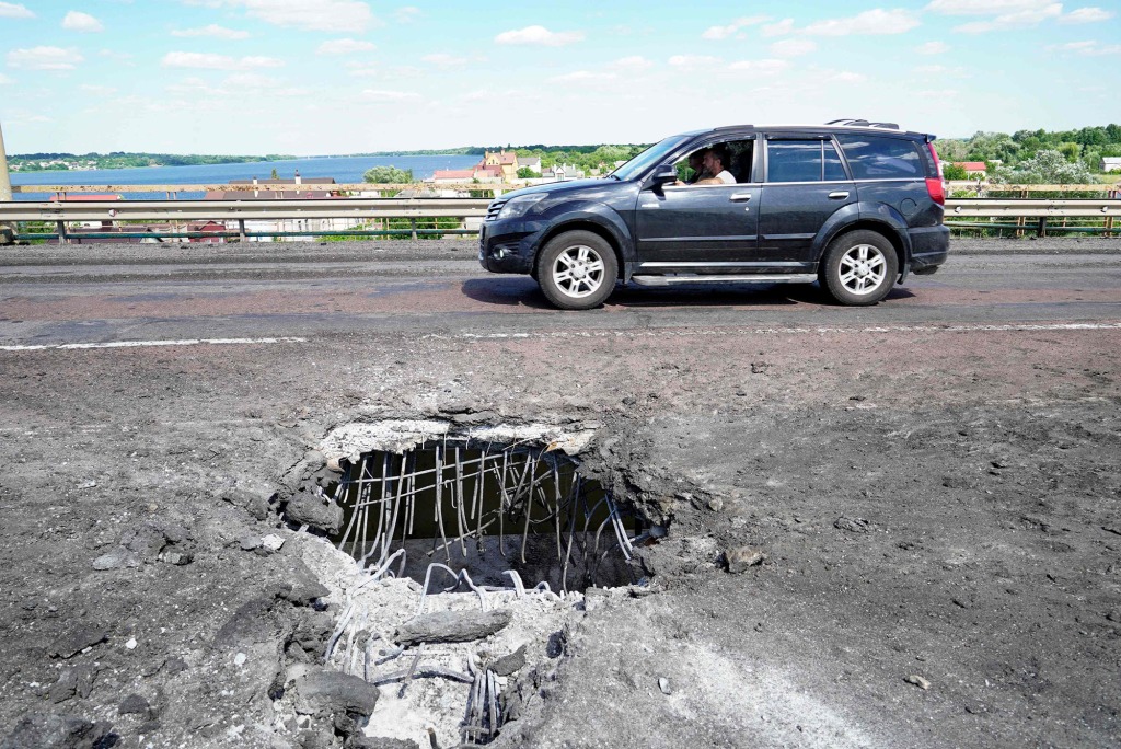 A car moving past a crater on Kherson's Antonovsky bridge across the Dnipro river caused by a Ukrainian rocket strike, amid the ongoing Russian military action in Ukraine.