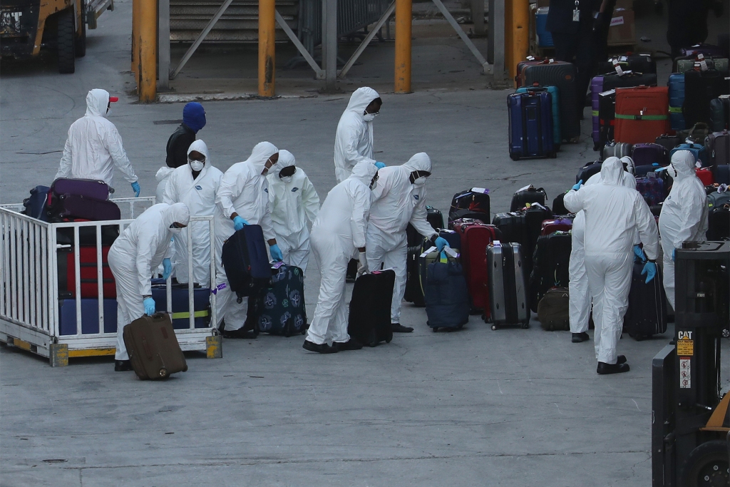 Worker dressed in hazmat suits take the luggage of off the Zaandam cruise ship after it arrived at Port Everglades.