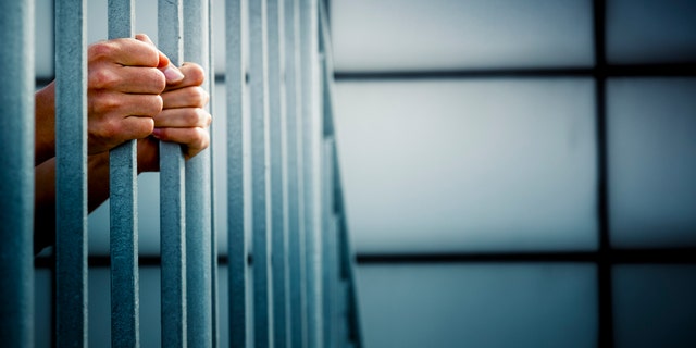 A prisoner behind the jail cell bars .