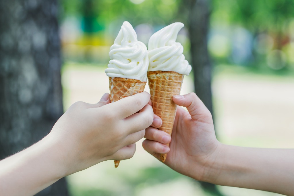 Two cones with creamy ice cream in children's hands.