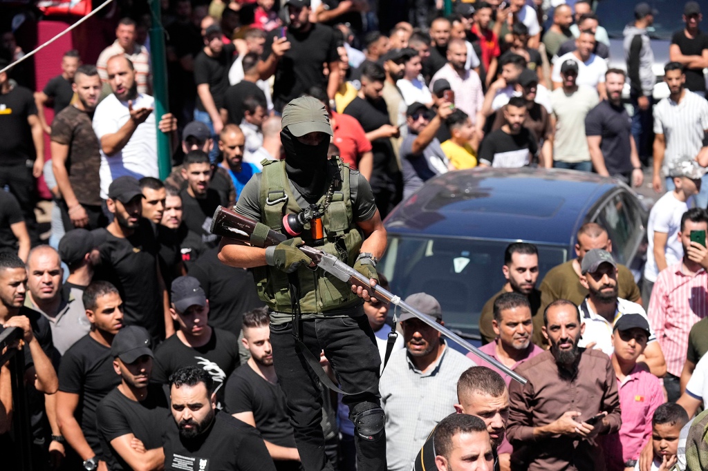 A gunman stands guard as Palestinian mourners gather for the funerals.