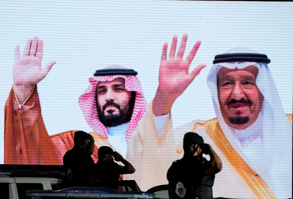 Saudi special forces salute in front of a screen displaying images Saudi King Salman, right, and Crown Prince Mohammed bin Salman