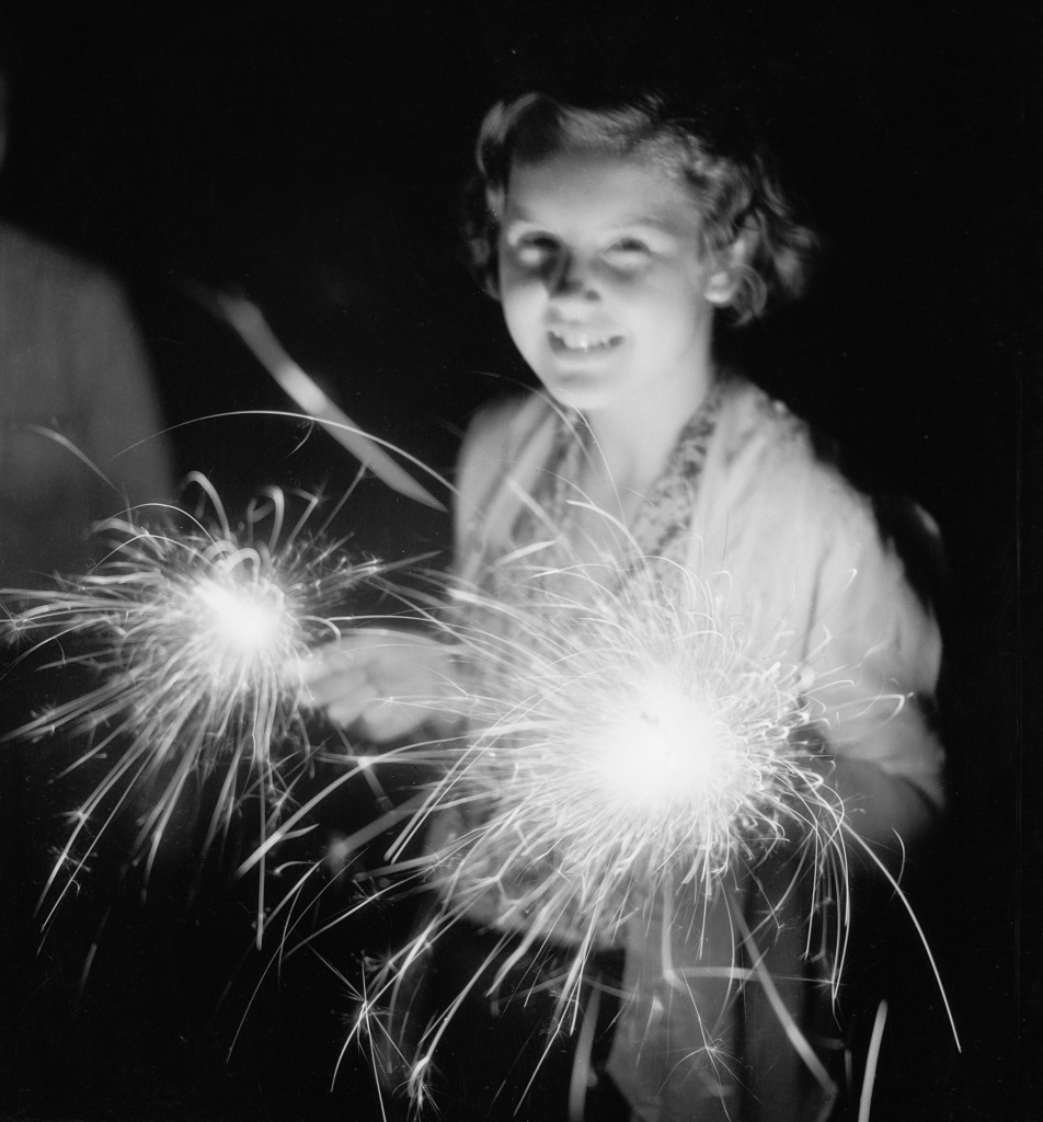 A girl holds two sparklers during a July 4th celebration, circa 1930.