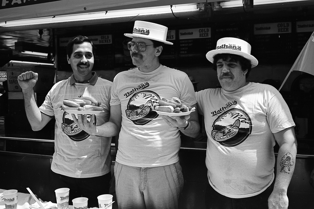 Three male contestants from Nathan's Hot Dog Eating Contest at Coney Island, New York, pose with plates of hot dogs, circa July 4, 1987. 