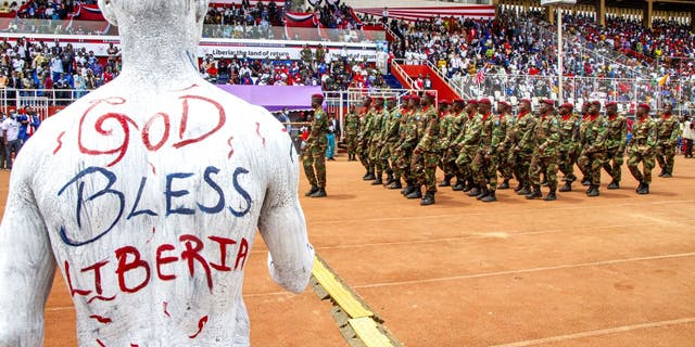 A Liberian artist paints his shirt with the national colours and the words 'God Bless Liberia' on his back during the military parade at the Liberia Bicentennial Celebration on February 14, 2022, in Monrovia 