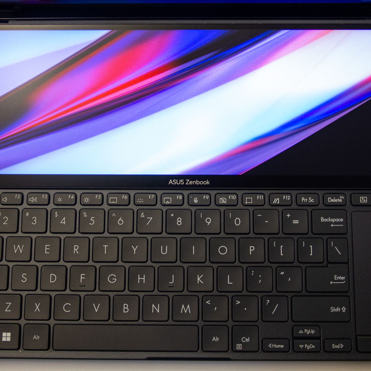 The keyboard deck of the Asus Zenbook Pro Duo 14 seen from above. The ScreenPad displays a multicolor background with a task bar on the left side.