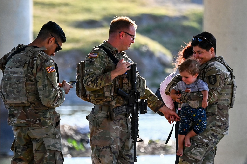 US Border Patrol and National Guard troops play with a migrant child as a group of migrants are apprehended in Eagle Pass, Texas, near the border with Mexico on June 30, 2022.