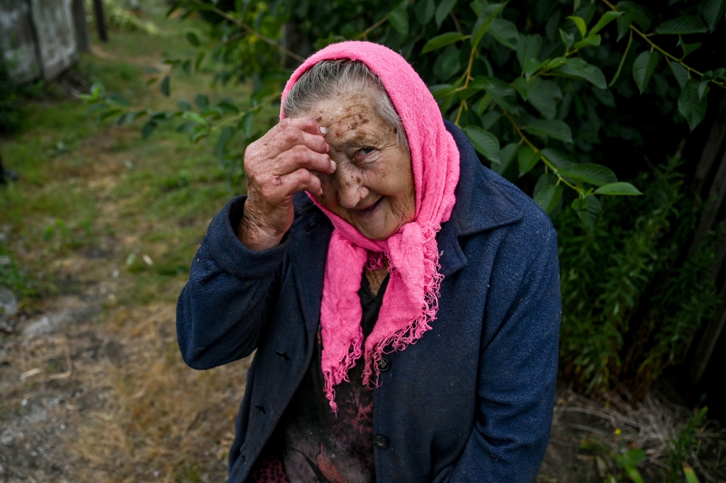 An elderly woman makes a sign of the cross in Prymorske village shelled by the Russian troops